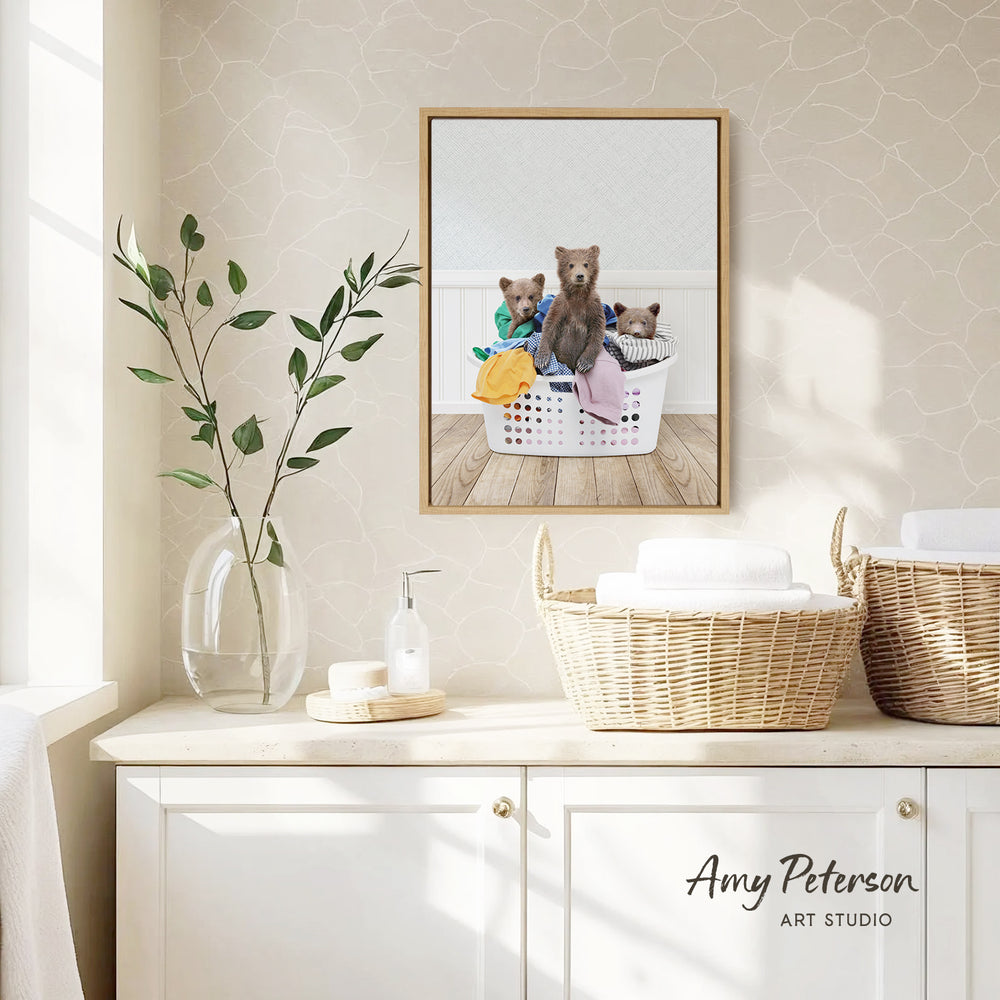 a framed picture of three bears sitting in a laundry basket, placed on a white cabinet in a bathroom setting.