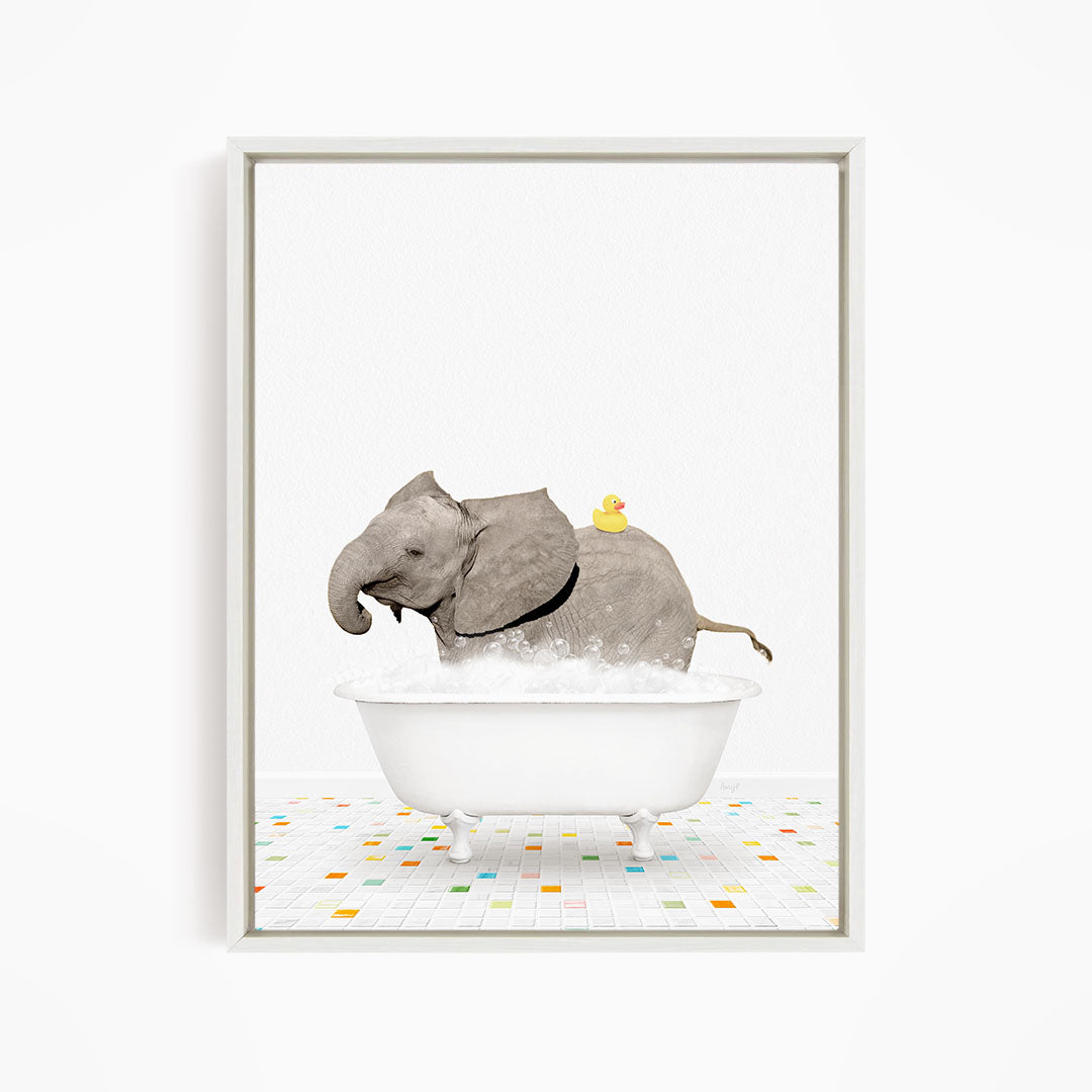 A gray elephant is standing in a white bathtub filled with bubbles, with a yellow rubber duck perched on its back.
