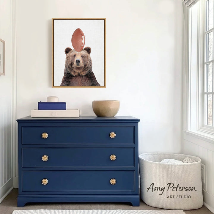 a blue dresser with a framed picture of a bear wearing a football on top of it. The dresser is situated in a room with white walls and a window.