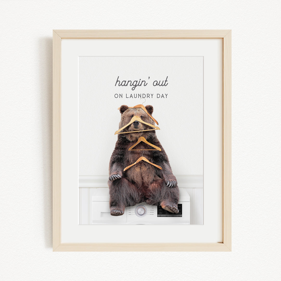A framed image of a bear sitting on a washing machine, with a humorous caption that reads "hangin' out on laundry day".