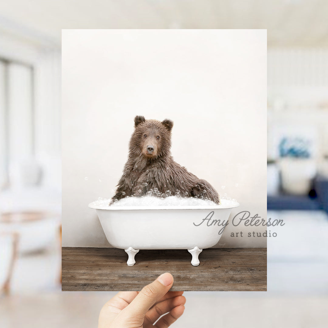 a hand holding up a photo of a bear in a bathtub