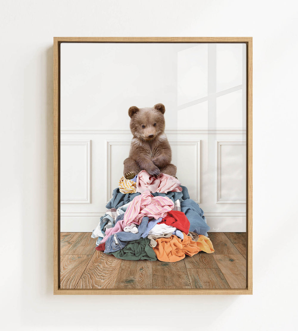 A teddy bear sitting atop a pile of clothes on a wooden floor.