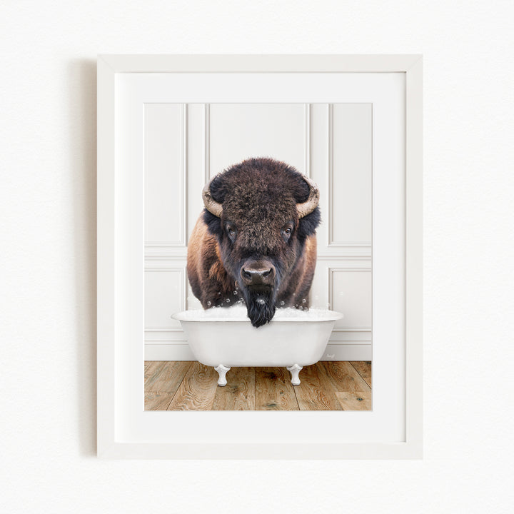 A buffalo with a black mane and nose is standing in a white bathtub filled with water, appearing to be enjoying a bath.