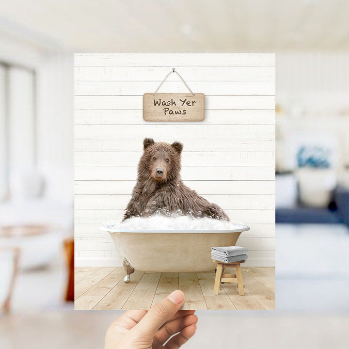 A brown bear sitting in a bathtub filled with bubbles, with a sign above that says "Wash Your Paws".