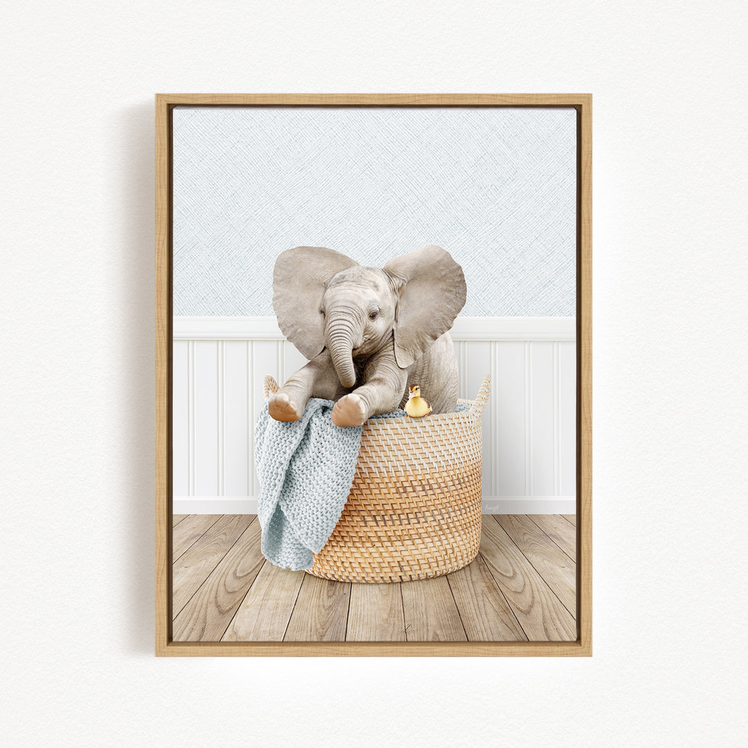 A baby elephant sitting in a woven basket, surrounded by a blue blanket and a yellow toy.