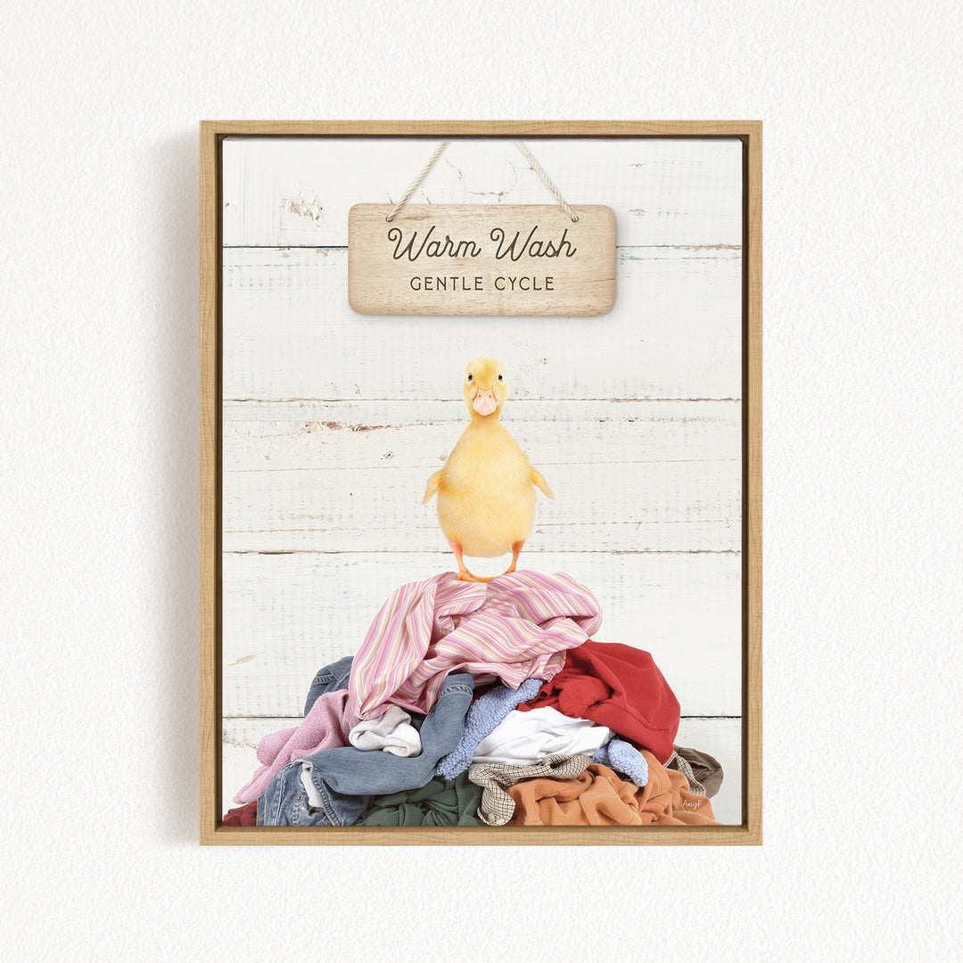 A yellow duck standing on a pile of clothes, with a wooden sign above that reads "Warm Wash Gentle Cycle".
