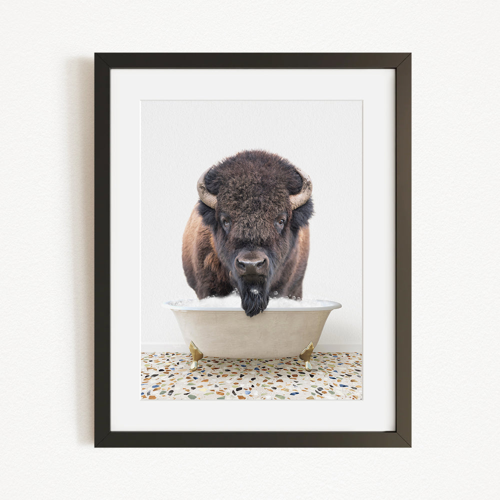 A buffalo with a long, shaggy mane is standing in a white bathtub filled with water, with a speckled floor beneath it.