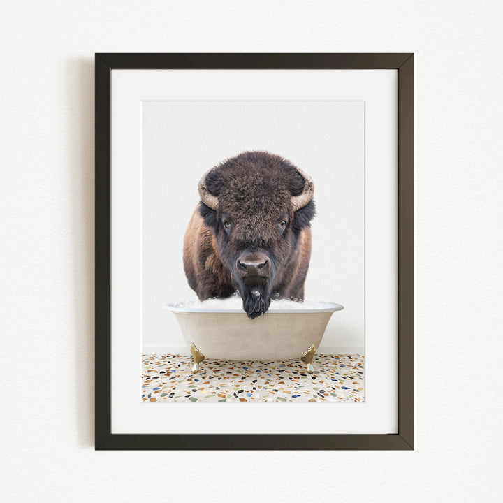 A buffalo with a long, shaggy mane is standing in a white bathtub filled with water, with a speckled floor beneath it.