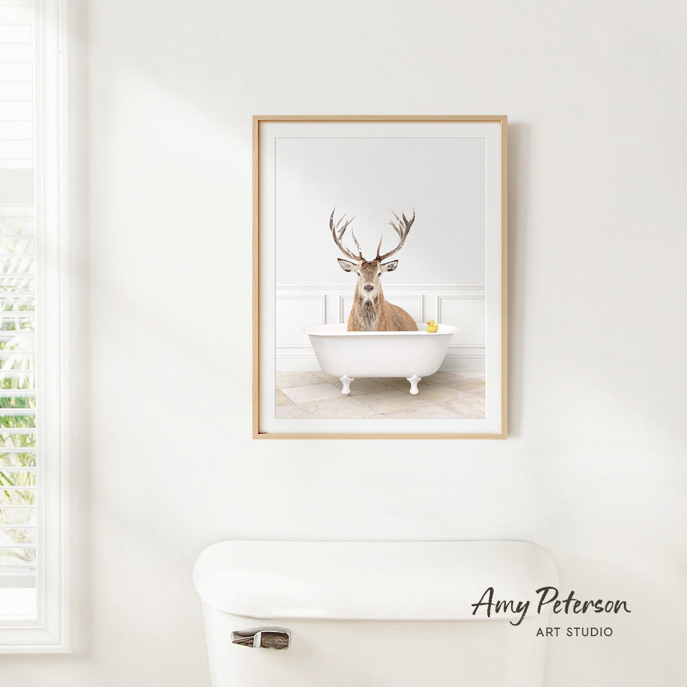 A framed image of a deer sitting in a bathtub, with a yellow rubber duck floating in the water.