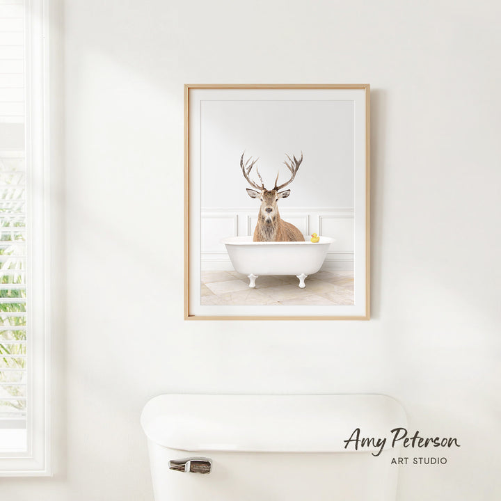 A framed image of a deer sitting in a bathtub, with a yellow rubber duck floating in the water.
