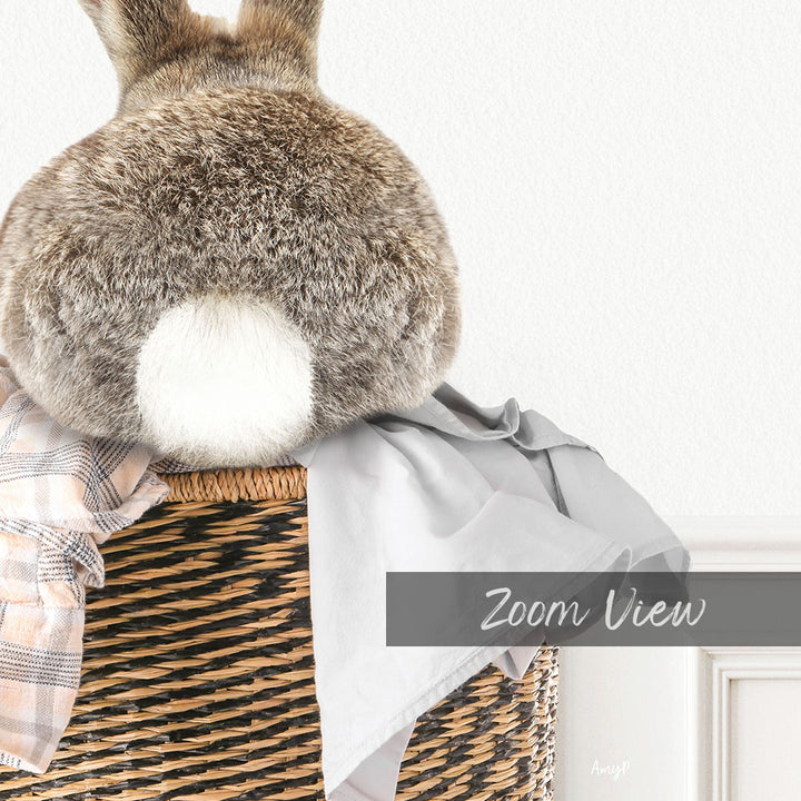 A fluffy gray rabbit sits in a woven basket, with a gray blanket and a white wall in the background.