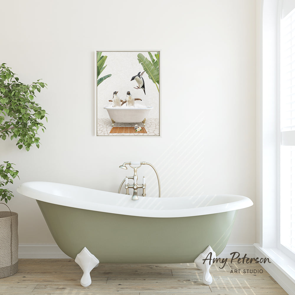 A green clawfoot bathtub with a white interior sits in a bright, airy bathroom, with a framed image of penguins in a bathtub hanging on the wall above it.