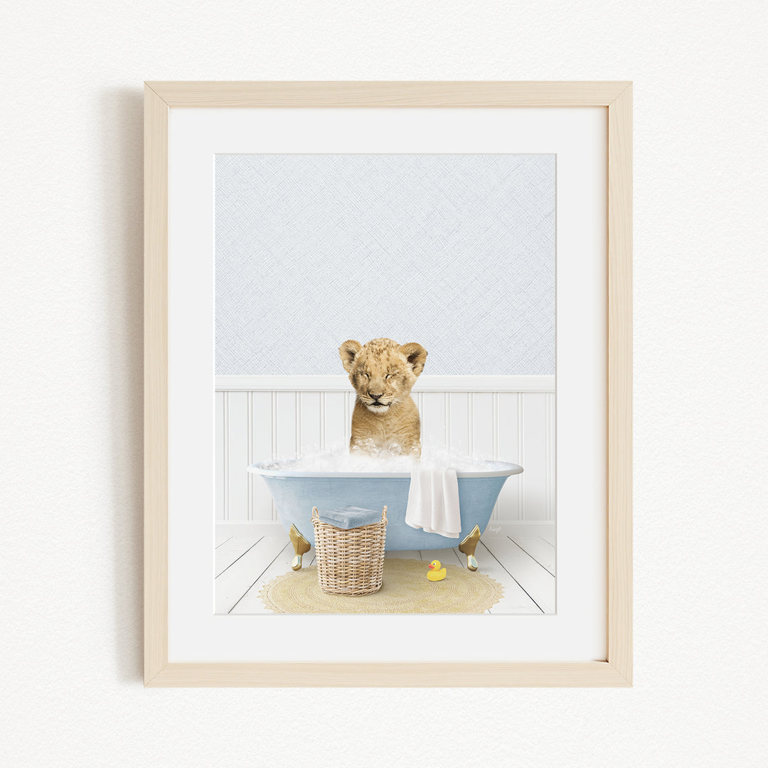 A young lion cub sitting in a blue bathtub filled with water, surrounded by rubber ducks and a basket.