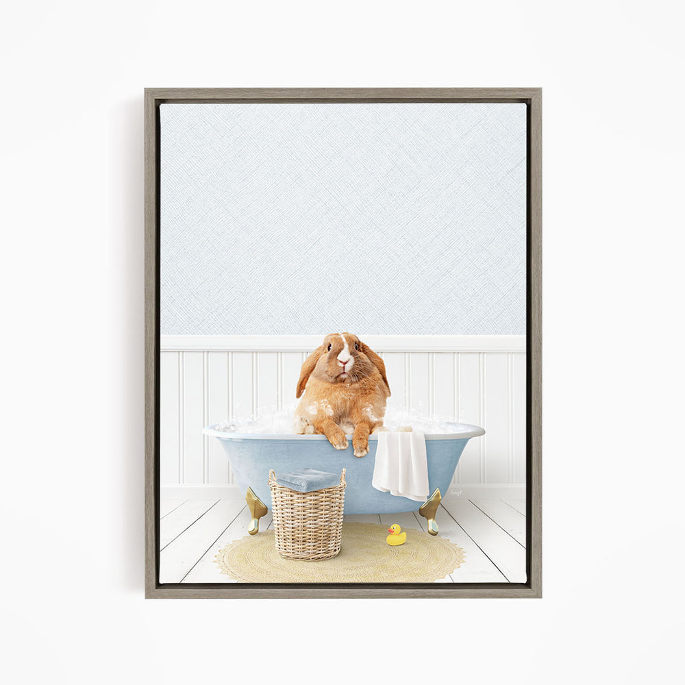 A brown rabbit sitting in a blue bathtub filled with bubbles, surrounded by a yellow rubber duck and a basket of bath toys.