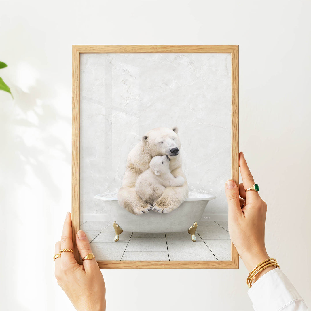 A person's hands are holding a framed picture of a polar bear and its cub sitting in a bathtub.