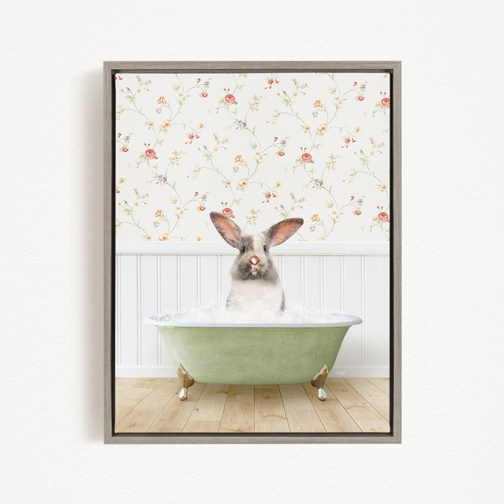 A white and brown rabbit sitting in a green bathtub filled with water, with a floral wallpaper in the background.