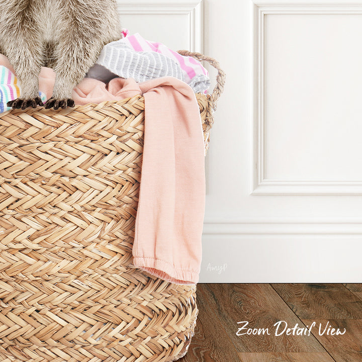 A woven basket filled with clothes and a pink towel, placed on a wooden floor against a white wall.