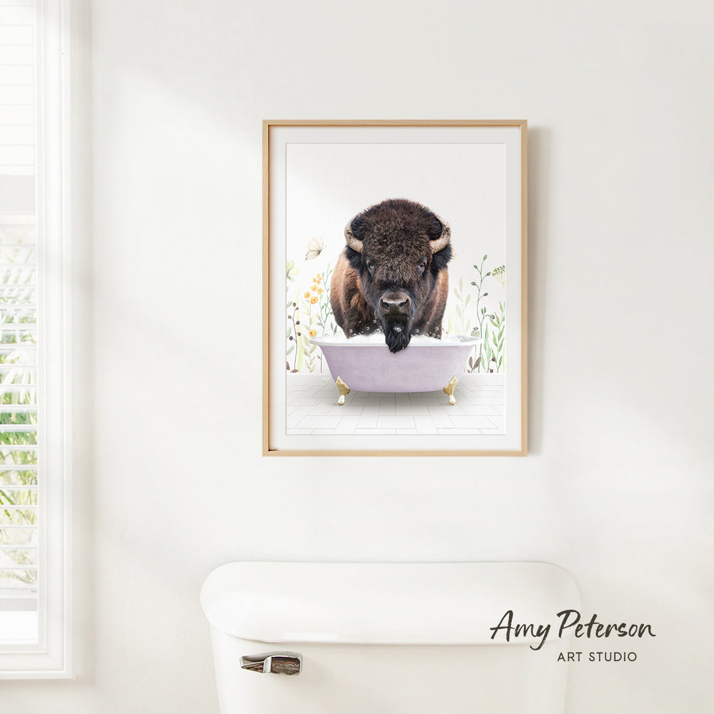 A framed print of a buffalo standing in a bathtub is hanging on a white wall.