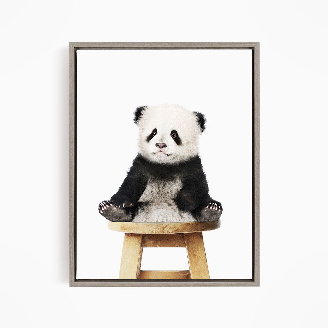 A cute panda sitting on a wooden stool against a white background.