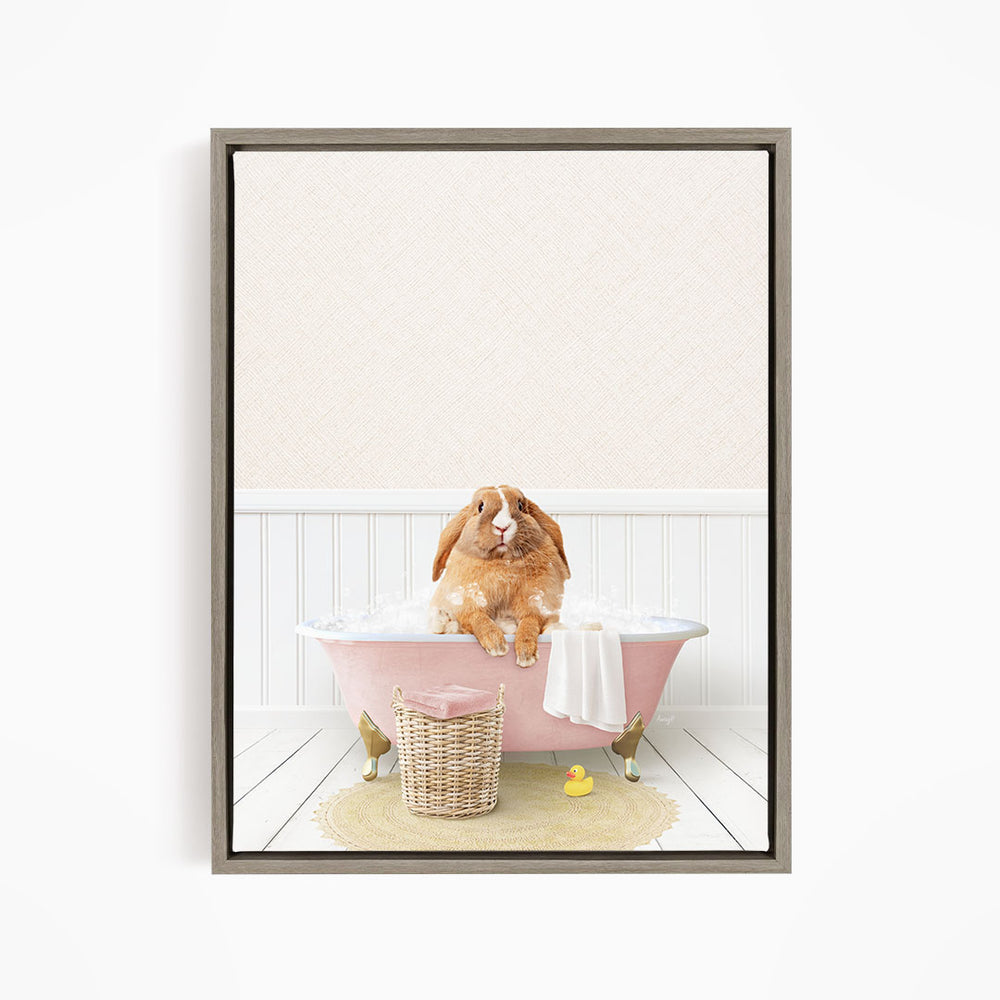 A brown rabbit sitting in a pink bathtub filled with bubbles, surrounded by a yellow rubber duck and a white towel.