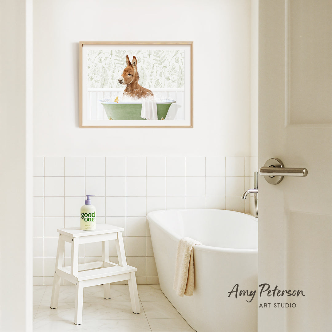 A framed painting of a dog sitting in a bathtub is hanging on a white tiled wall above a white bathtub in a bathroom.