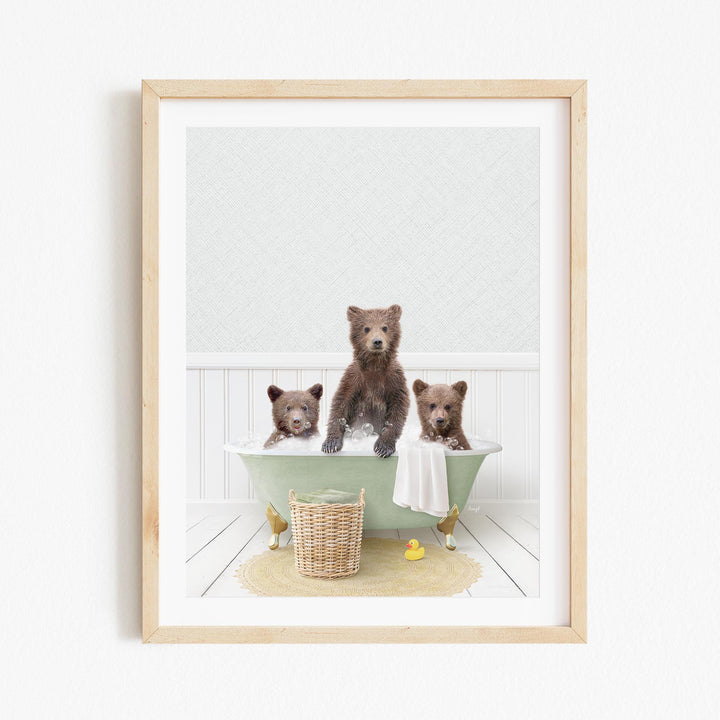 A framed image depicting three brown bears sitting in a green bathtub, with a basket of toys and a towel nearby.