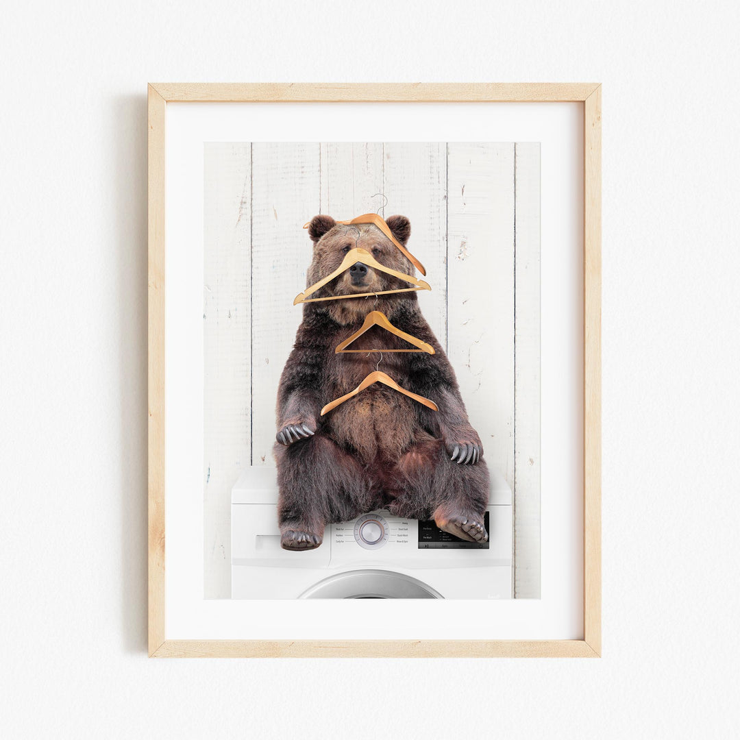 A brown bear sitting on a washing machine, surrounded by hanging clothes.