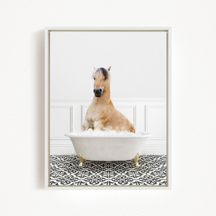 A light brown horse is sitting in a white bathtub filled with bubbles, surrounded by a black and white patterned floor.
