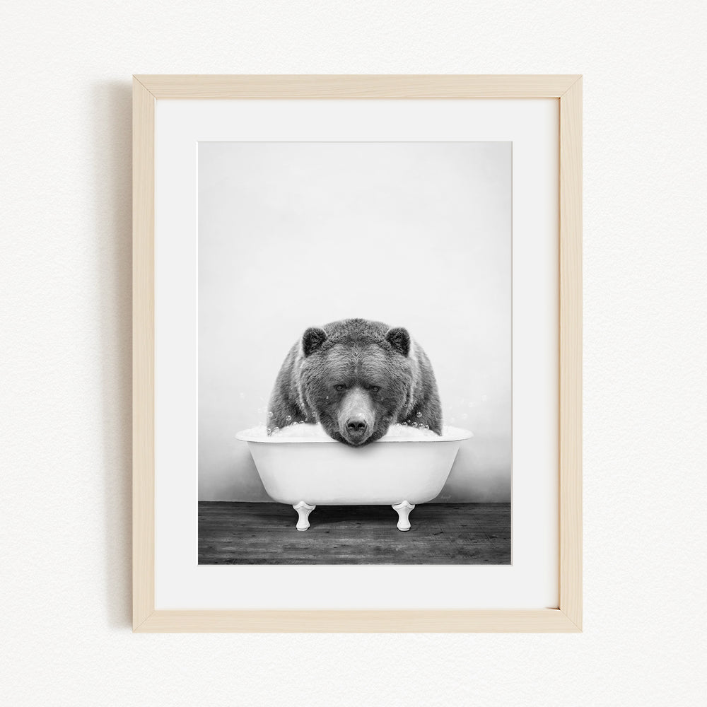 A black and white photograph of a bear sitting in a bathtub filled with water.