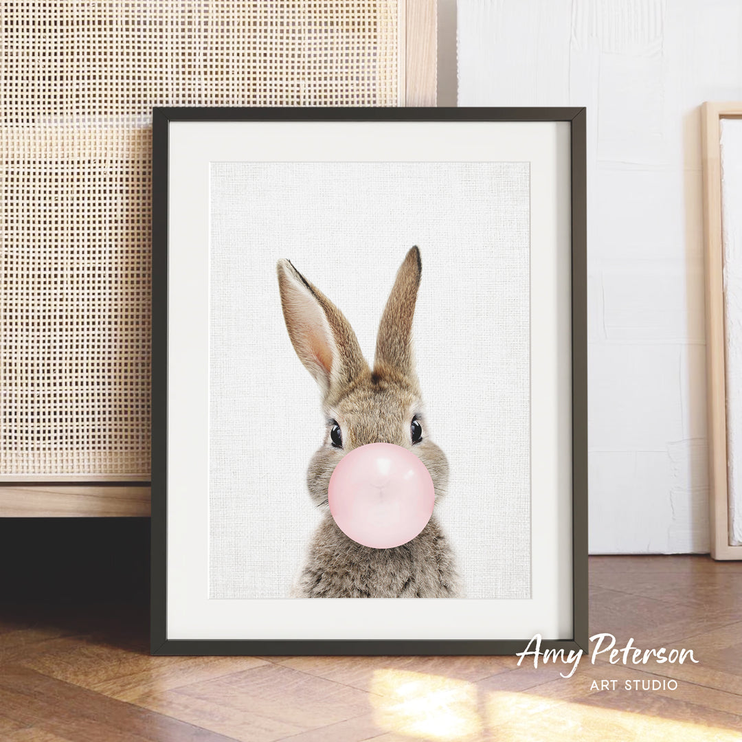 A framed image of a rabbit blowing a bubble with a pink bubble gum bubble.