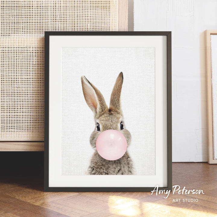 A framed image of a rabbit blowing a bubble with a pink bubble gum bubble.