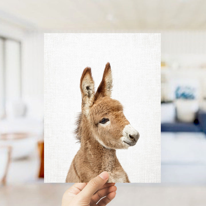 A hand is holding up a square print of a donkey's head against a white background.