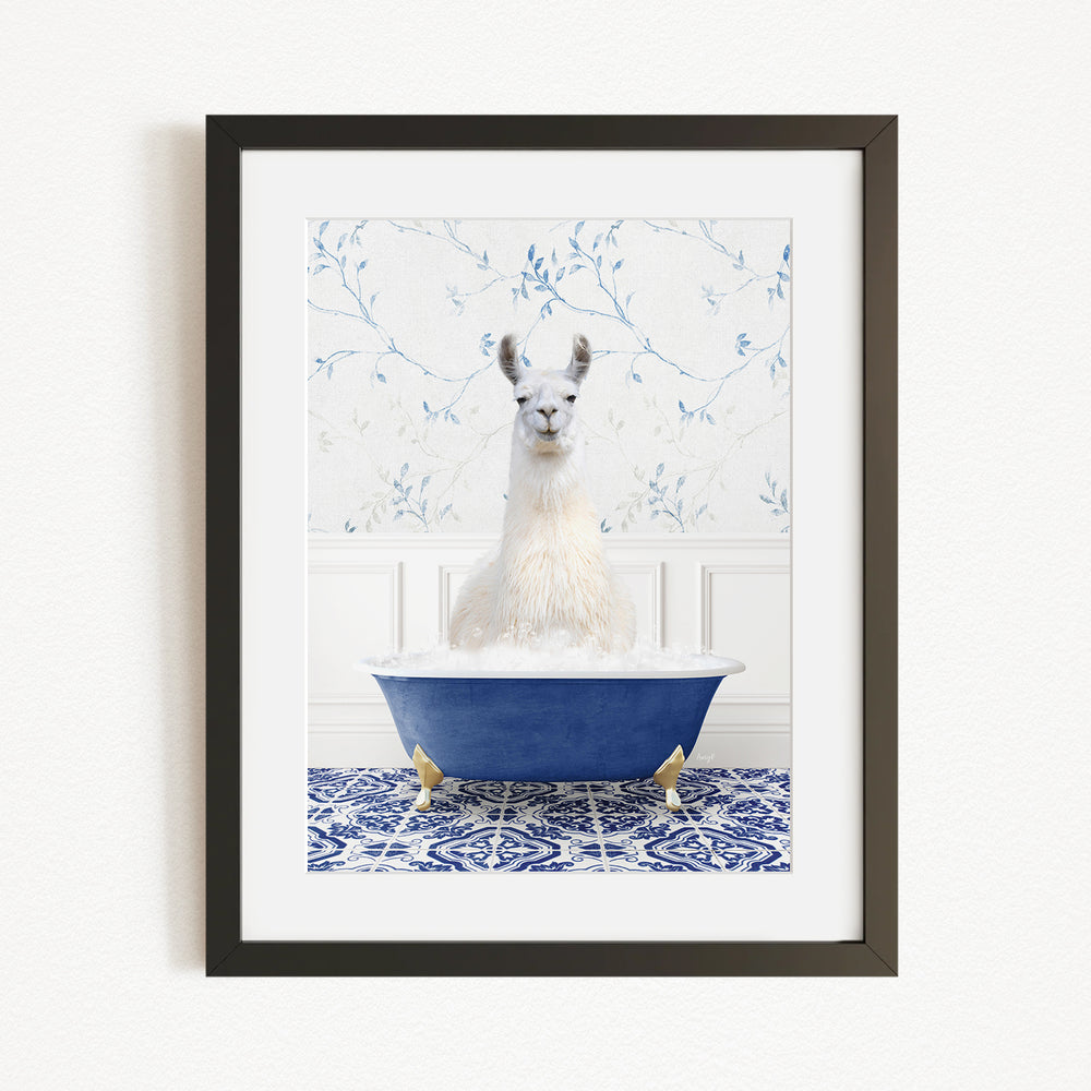 A white llama sitting in a blue bathtub filled with bubbles, against a white wall with a blue floral pattern.