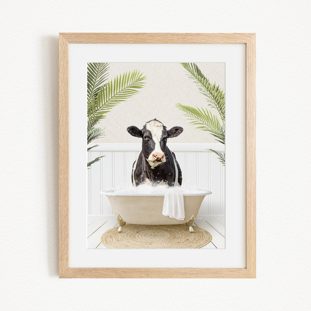 A black and white cow is sitting in a bathtub filled with water, surrounded by green palm leaves.