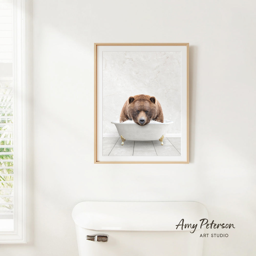 A framed image of a brown bear sitting in a bathtub is hanging on a white wall.