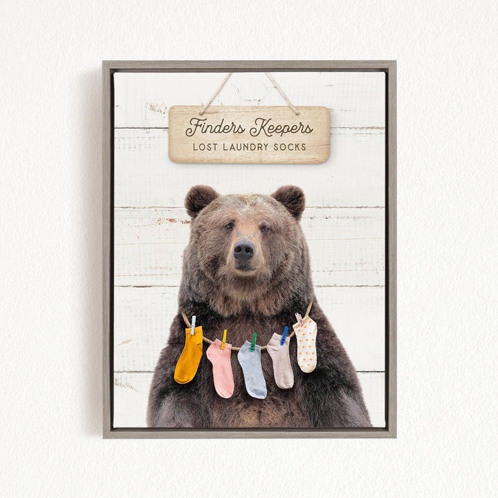 A framed image of a brown bear wearing colorful socks hanging on a clothesline, with a sign above that reads "Finders Keepers Lost Laundry Socks".