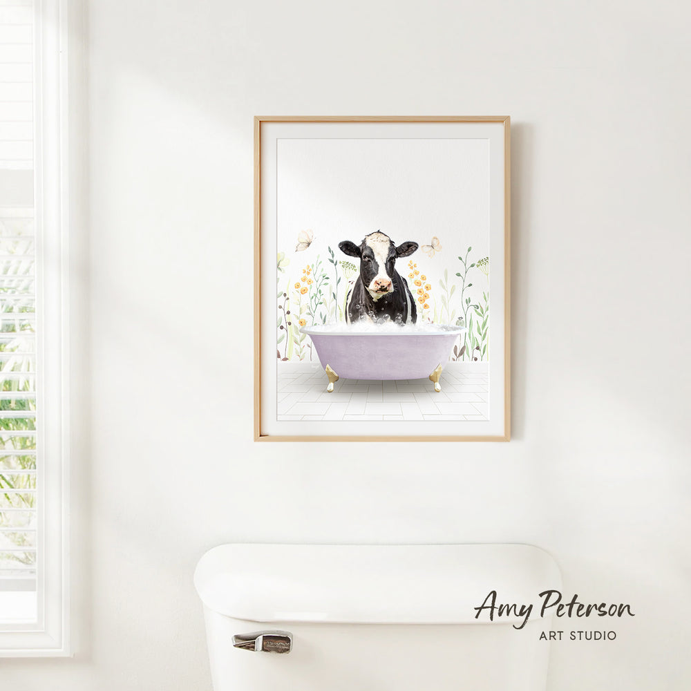 A framed print of a cow sitting in a bathtub is hanging on a white wall.