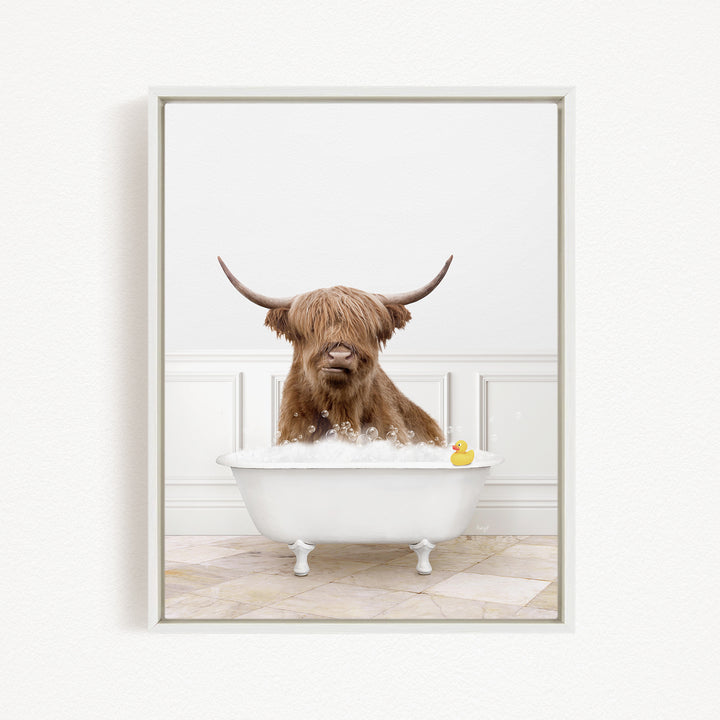 A brown cow with long horns is sitting in a white bathtub filled with bubbles, with a yellow rubber duck floating in the water.
