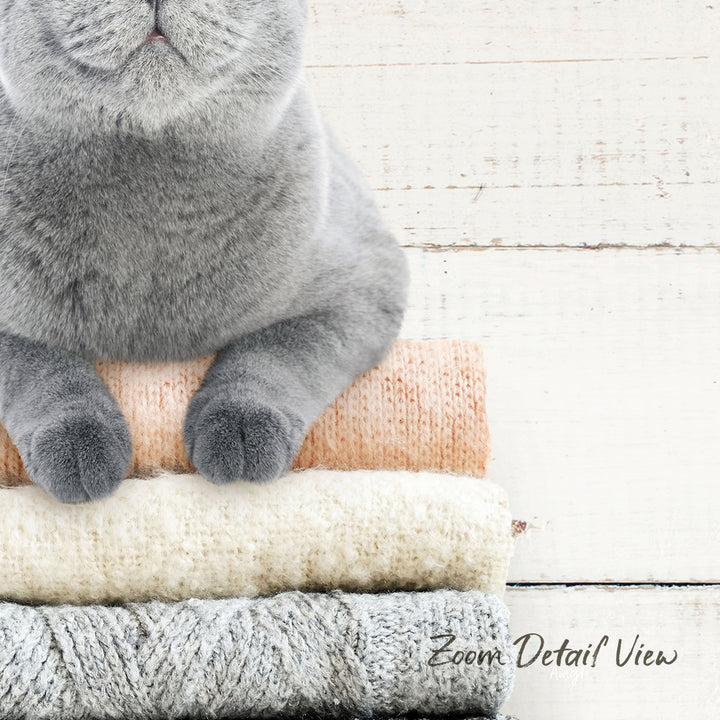 A gray cat sitting on top of a stack of various colored blankets and towels.