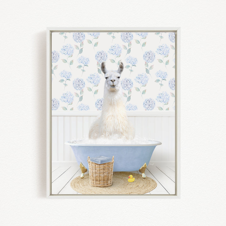 A white llama sitting in a blue bathtub filled with bubbles, surrounded by a wicker basket and a yellow rubber duck.