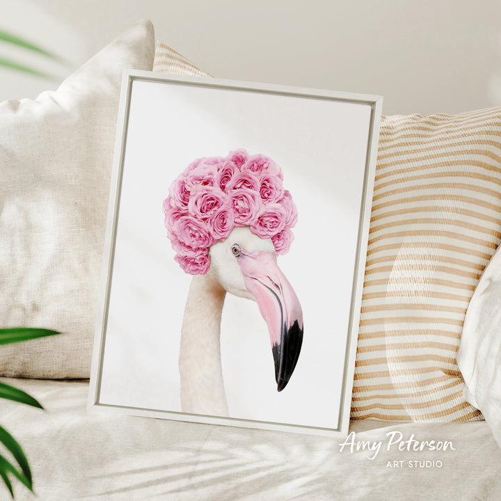 A framed image of a flamingo with pink flowers on its head, displayed on a bed with striped pillows.