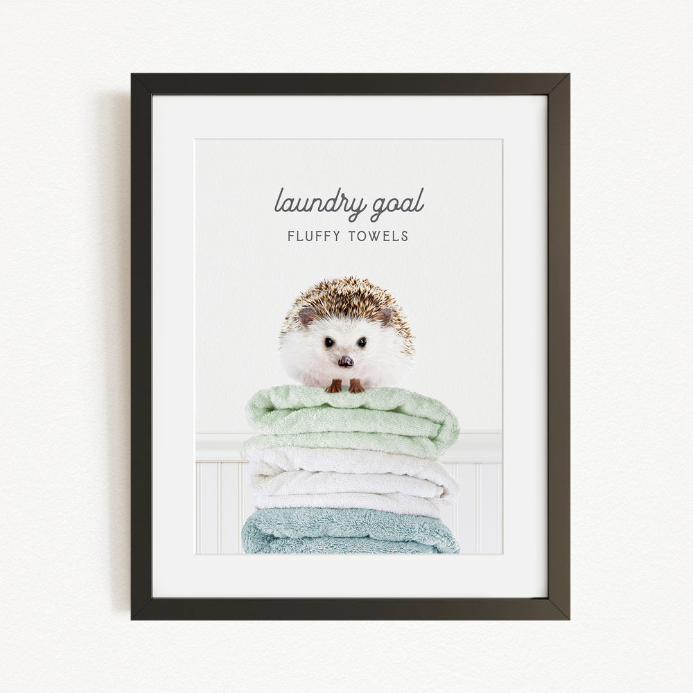 A framed image of a hedgehog sitting atop a stack of fluffy towels, with the text "laundry goal" and "fluffy towels" written above it.