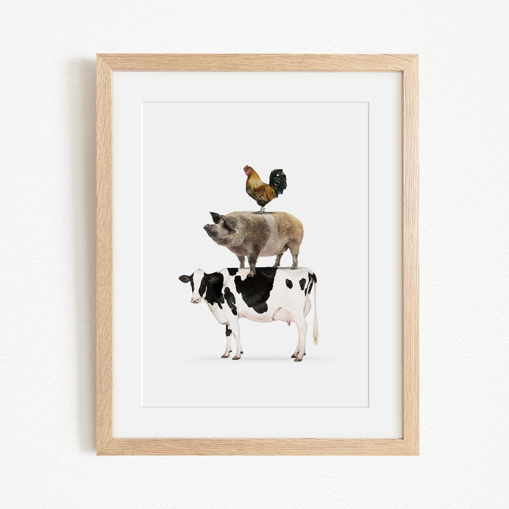 A framed illustration depicting a pig, cow, and rooster standing on top of each other.