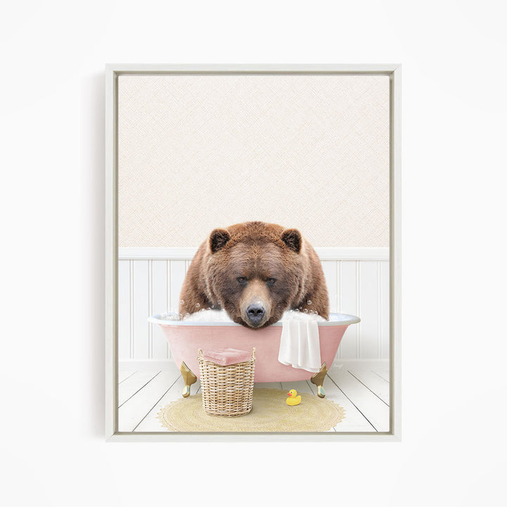 A brown bear is sitting in a pink bathtub filled with water, surrounded by a yellow rubber duck and a white towel.