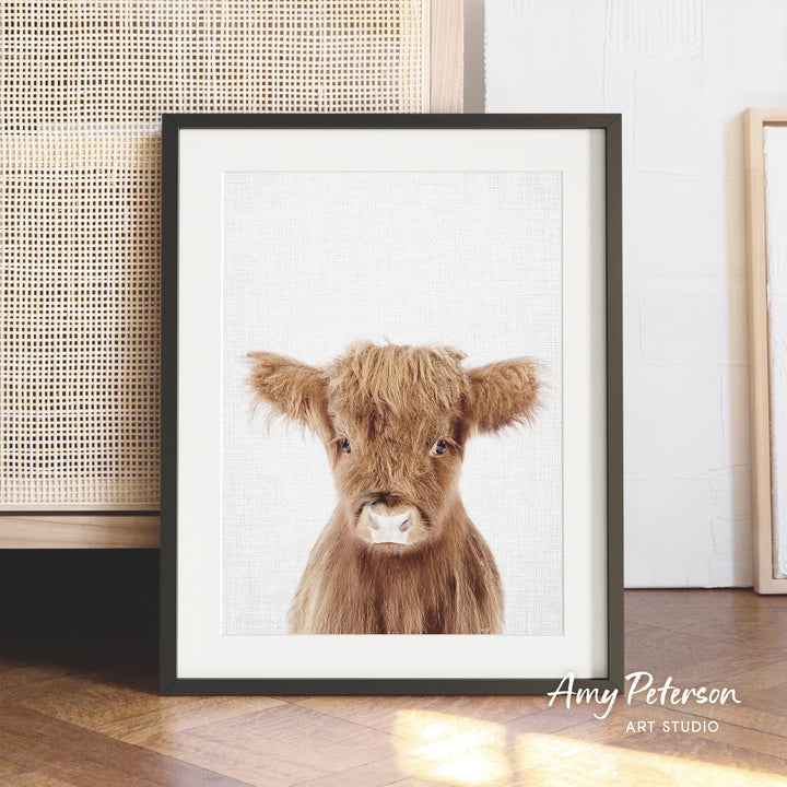 A framed image of a brown cow with shaggy fur is displayed on a wooden floor in front of a woven basket.