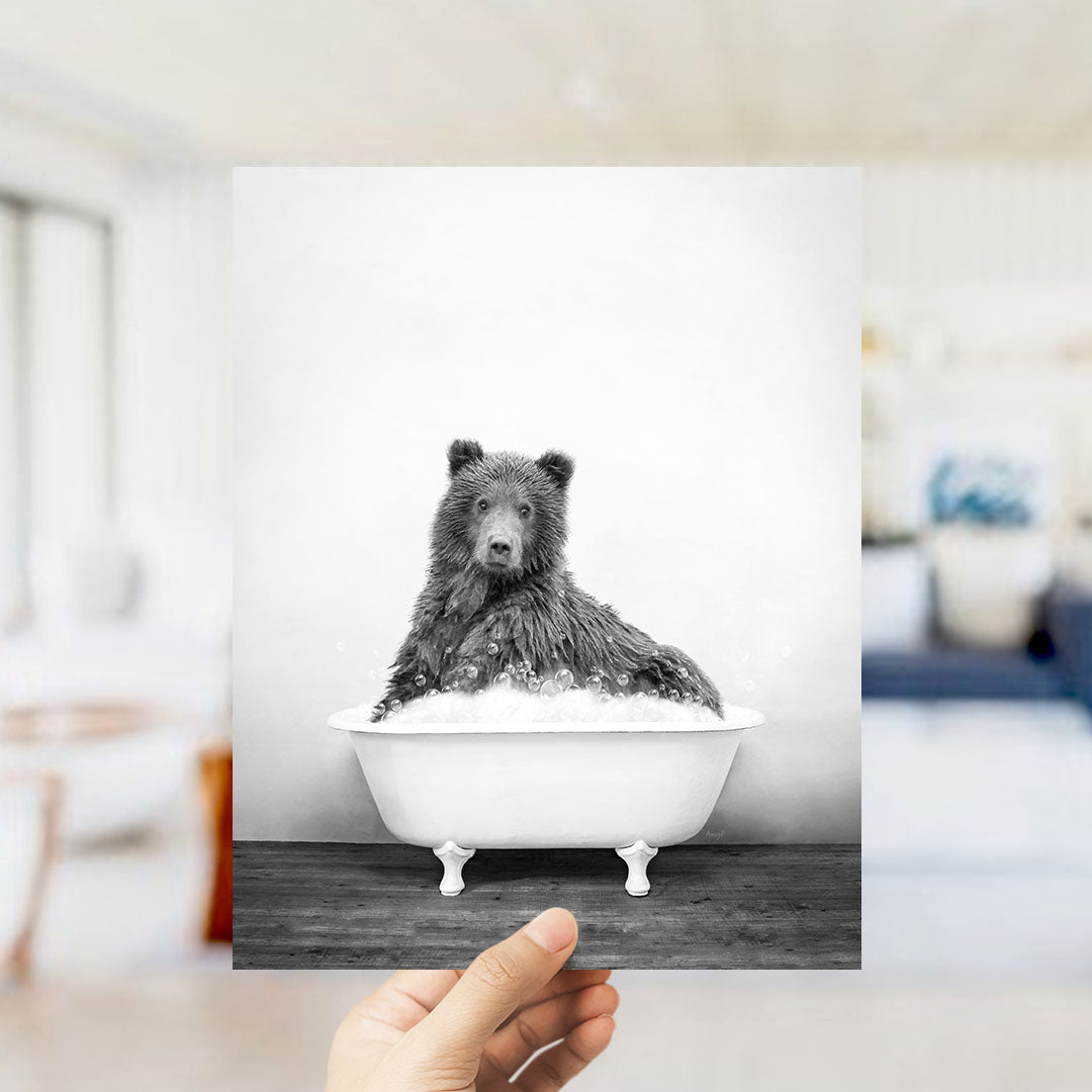 A black and white photograph of a bear sitting in a bathtub filled with water.