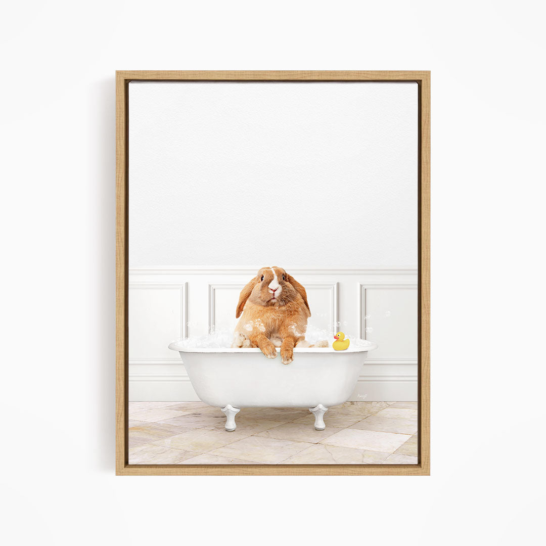 A brown rabbit sitting in a white bathtub filled with bubbles, with a rubber duck floating in the water.