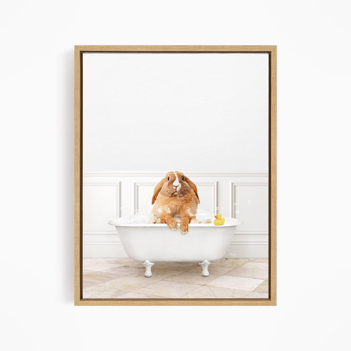 A brown rabbit sitting in a white bathtub filled with bubbles, with a rubber duck floating in the water.