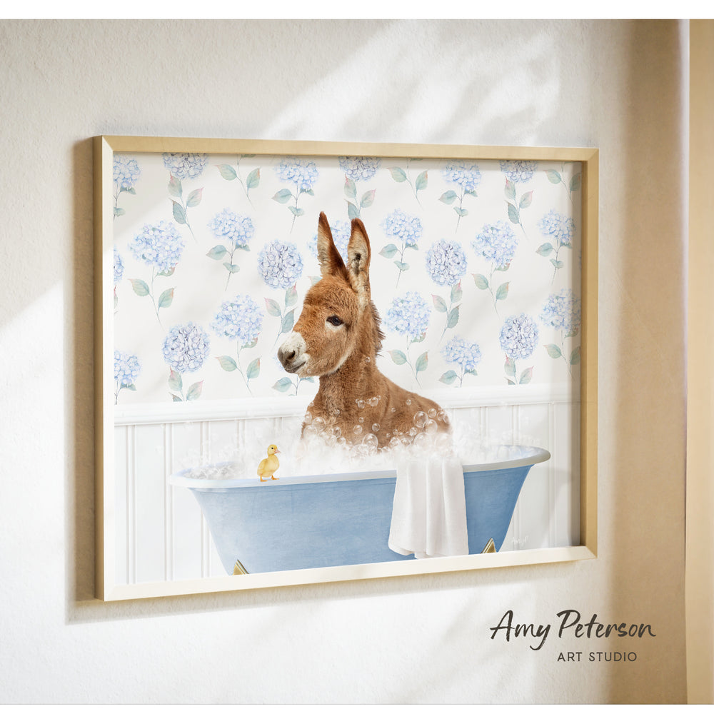 A donkey is sitting in a blue bathtub filled with bubbles, with a yellow duck nearby, against a backdrop of blue hydrangea flowers.