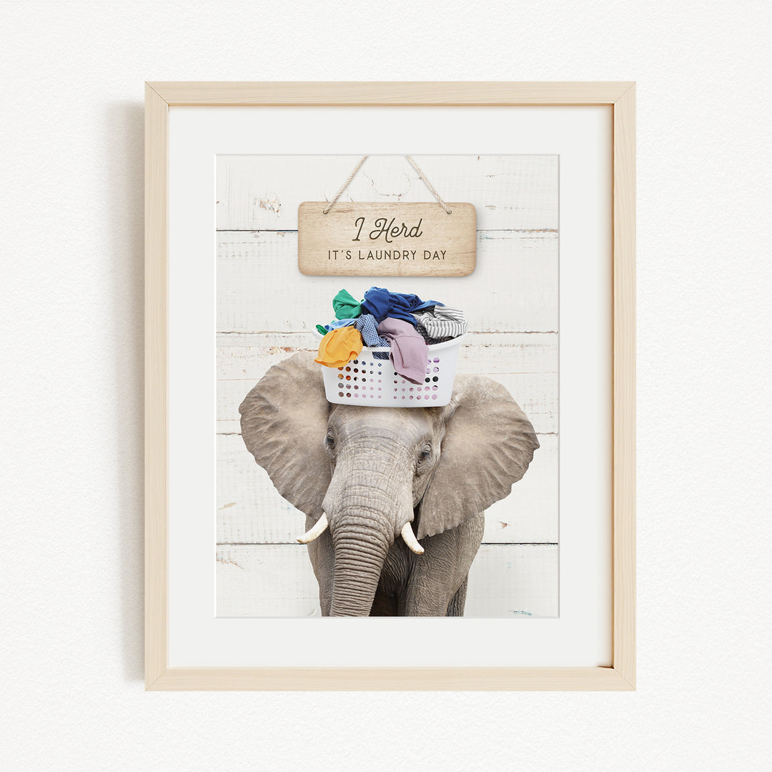 A framed image of an elephant holding a basket full of laundry, with a sign above it that says "I Harded It's Laundry Day".